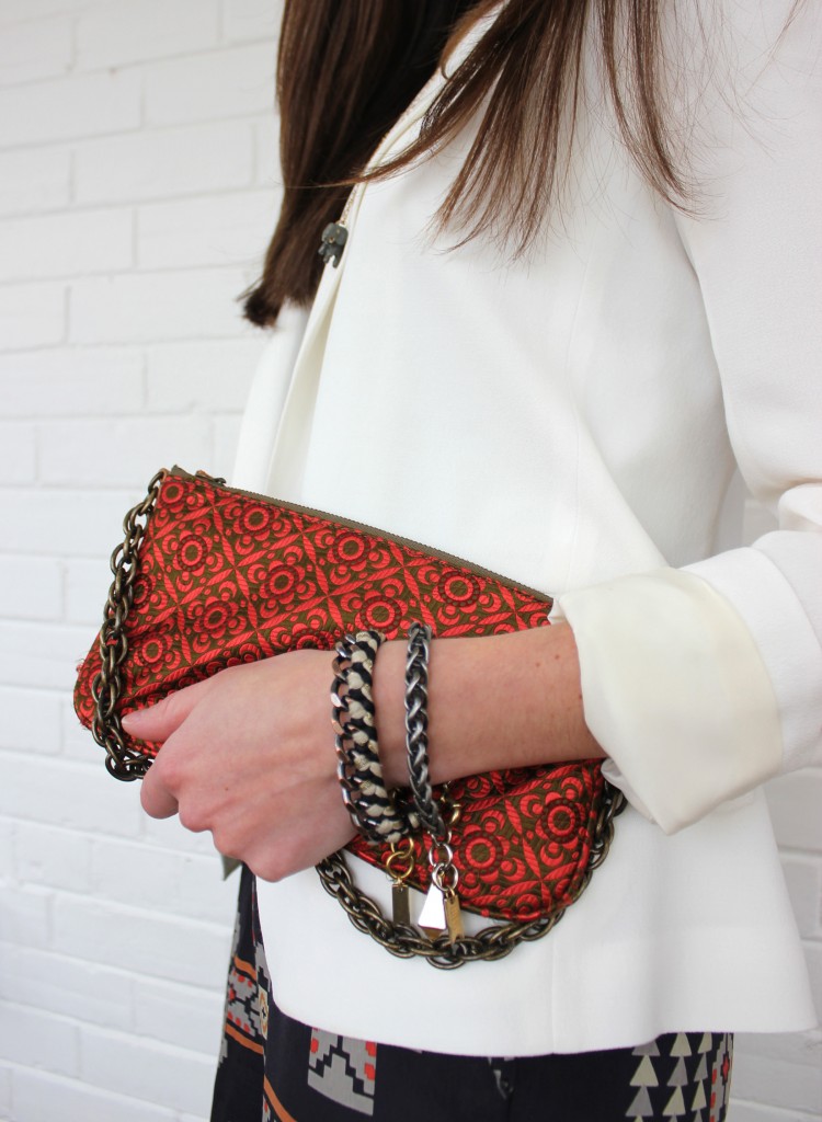 Girl holding red clutch, wearing white blazer.